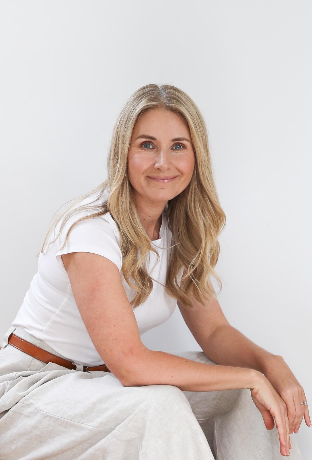 Magdalena Roze sitting and smiling, wearing a white top and white pants.
