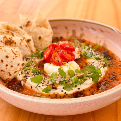 A bowl of Laksa Turkish Eggs with roti bread on the side and chilli slices on top of the eggs