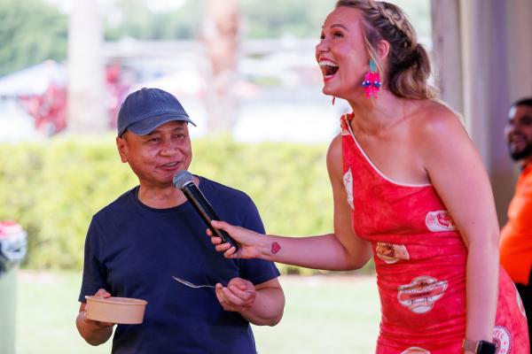 Amy Hetherington is interviewing and laughing with a man eating laksa