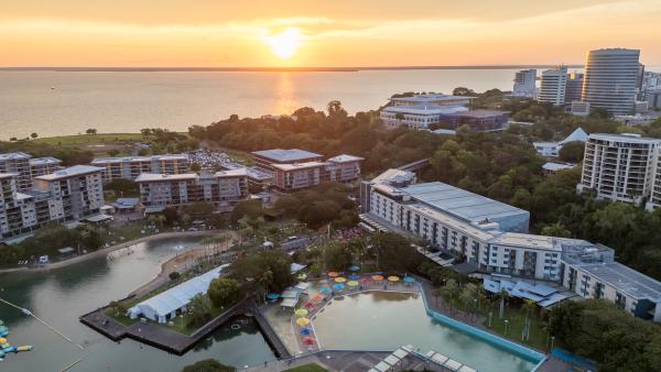 Drone image of the Darwin Waterfront area, showing the wave pool, lagoon, and the Laksa Festival setup. The sun is setting over the ocean in the background.