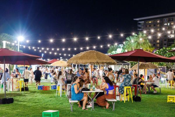 The Laksa Festival crowd sitting around picnic tables at night, under festoon lighting
