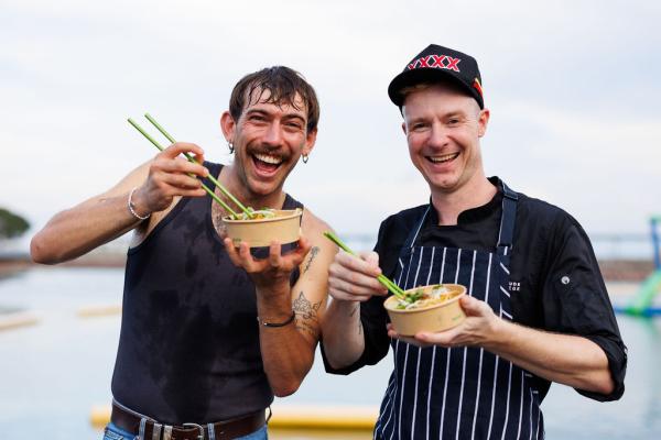 Outback Tom and the Outback Chef posing with their laksa dishes in front of the lagoon pool